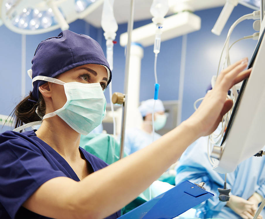 A masked nurse stands in the foreground and is operating a medical device