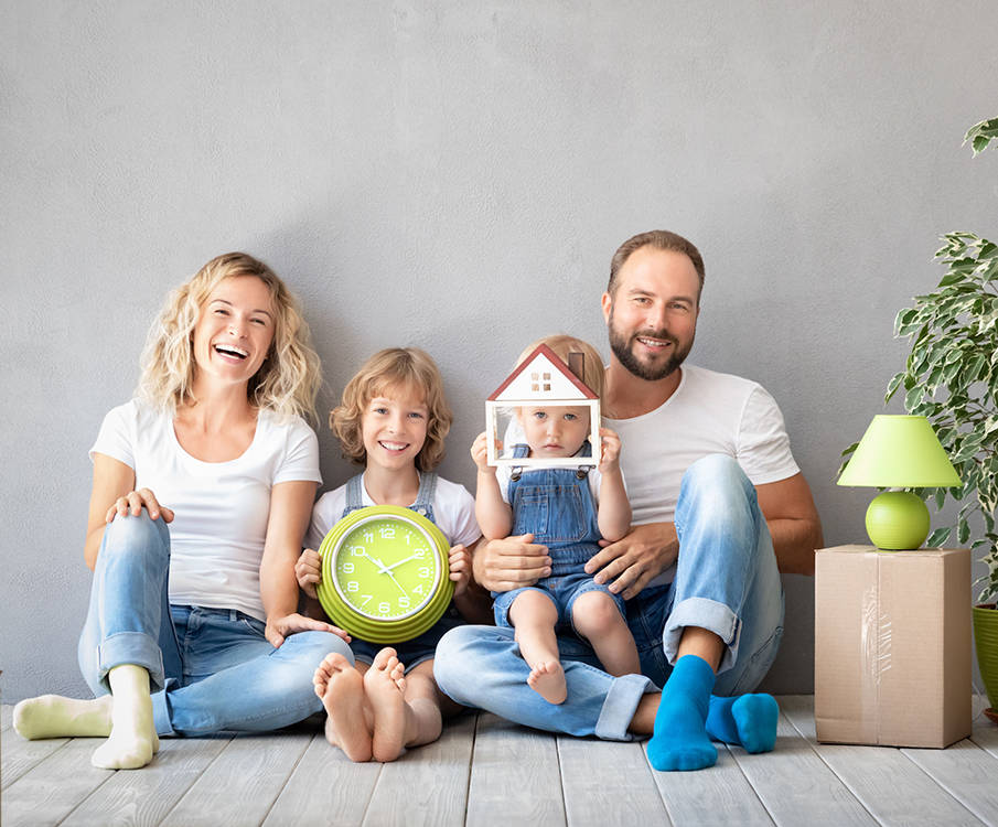 A happy family of four sits on the floor and the children have in their arms a clock and a wooden house